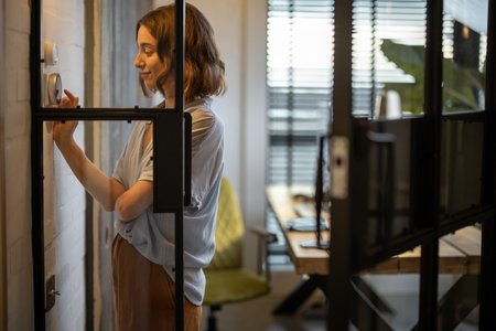 Young woman controlling room temperature with a smart thermostat at home. Home comfort and smart heating system conceptの写真素材