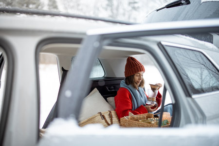 Woman have a coffee in car trunk in winter forestの写真素材