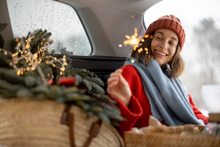 Woman smiling and looking at sparkler while sitting in car trunkの写真素材