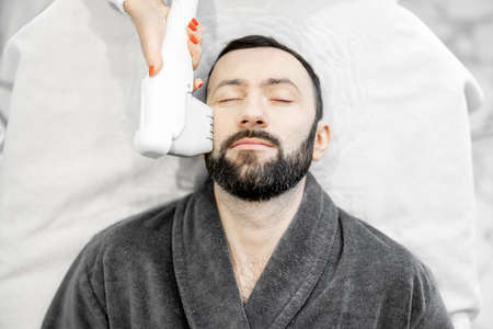 Man on ultrasound face lifting procedure in cosmetology salonの写真素材