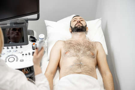 Doctor examining liver of male patient with ultrasound scan in clinicの写真素材