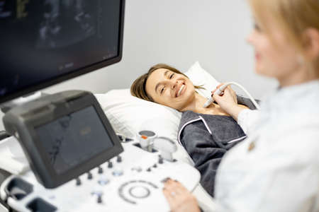 Doctor examining thyroid of female patient with ultrasound scan in clinicの写真素材