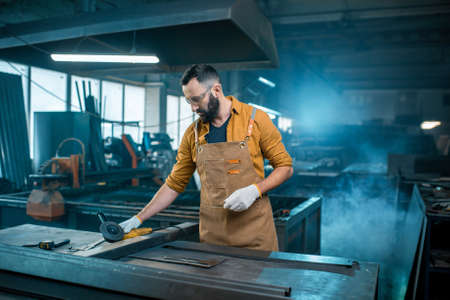 Metal industry worker dressed in work wear doing some metalwork, grinding steel product at the factory. Handsome artisan at the manufacturing of metal products. High quality photoの写真素材