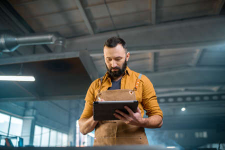 Metal industry worker dressed in work wear doing some metalwork, grinding steel product at the factory. Handsome artisan at the manufacturing of metal products. High quality photoの写真素材
