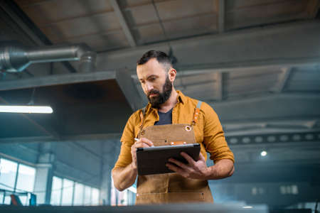 Metal industry worker dressed in work wear doing some metalwork, grinding steel product at the factory. Handsome artisan at the manufacturing of metal products. High quality photoの写真素材