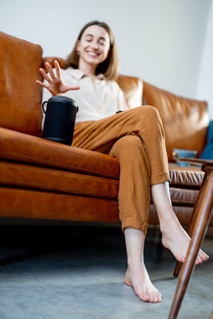Woman speaking with audio assistant column on sofa