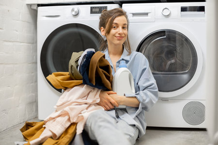 Woman with clean clothes and detergent in the laundry room at homeの写真素材
