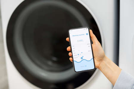 Woman controls washing machine with a smartphoneの写真素材