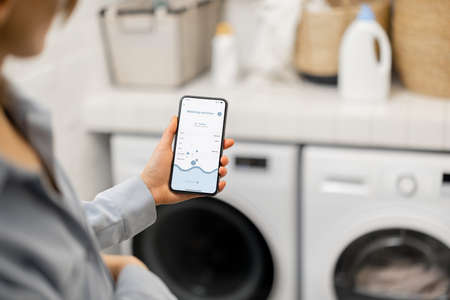 Woman controls washing machine with a smartphoneの写真素材