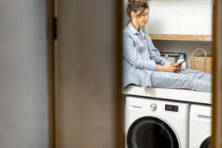 Woman with phone in the laundry roomの写真素材