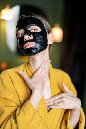 Woman in black facial mask doing neck massageの写真素材