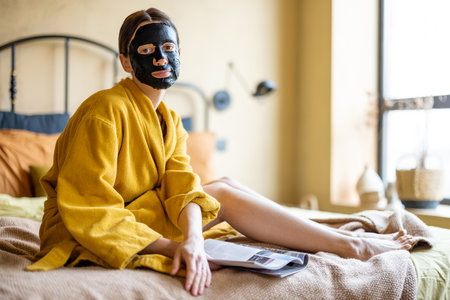 Woman with black cleansing mask on her face in bedroomの写真素材