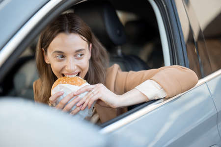 Happy woman eating a burger in the carの写真素材