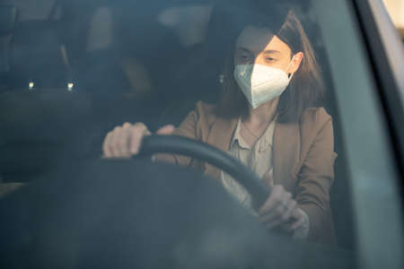 Woman driving car with protective mask on her face.の写真素材