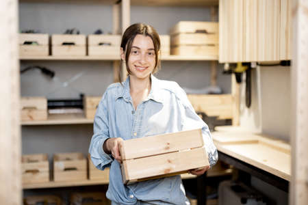 Portrait of a young handywoman holding wooden toolbox in the workshop. Concept of organization in home workshop or storageの写真素材