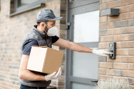 Courier wearing mask and gloves holds a parcel boxの写真素材