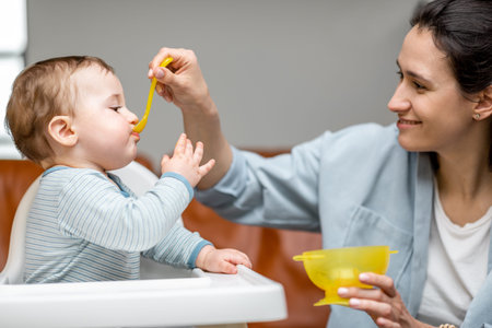 Mother feeding her one year baby boy with a spoon.