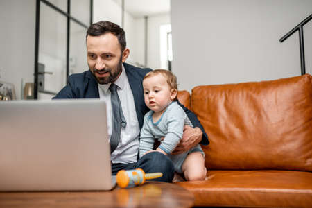 Young businessman dad working on a laptop at homeの写真素材