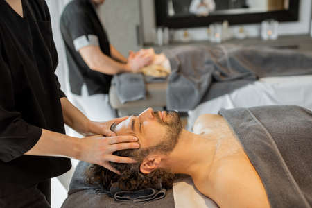 Two masseurs doing facial massage to a couple at Spa salonの写真素材