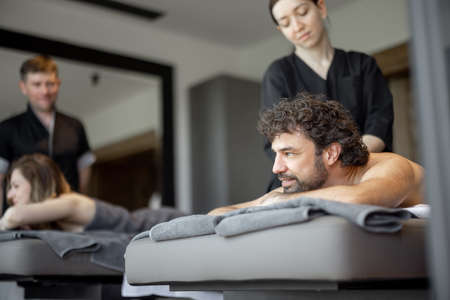 Beautiful couple lying in a spa salon enjoying getting deep back massage and relaxation.の写真素材