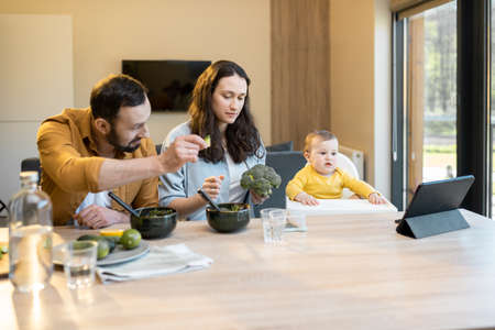 Young happy family with a one year baby boy during a lunch time at home. Concept of healthy vegan eating and happy parentingの写真素材