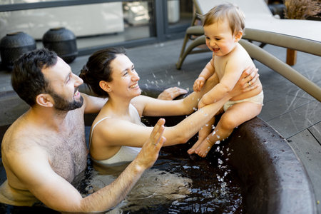 Young family relaxing with a little baby boy at spa, sitting in the hot vat outdoors. Family on vacation with a childの写真素材