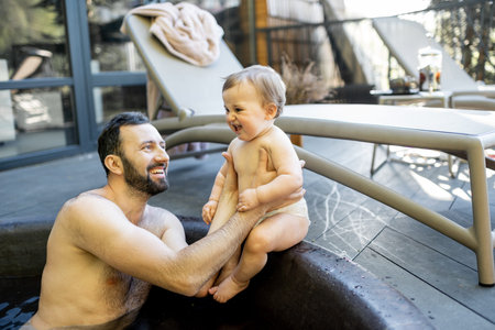 Father relaxing with a little baby boy at spa resort, sitting in the hot vat outdoors. Family on...