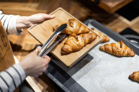 Housewife putting freshly baked croissants on a wooden tray, close-up. Home baking conceptの写真素材