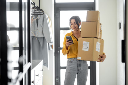 Young woman with parcels at the hallway at home, holds smart phone and checking goods. Concept of...