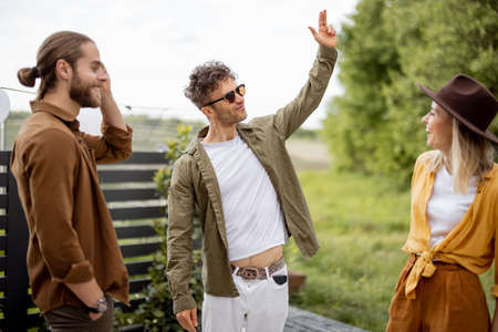 Young adult friends hang out, talking and having fun together at the beautiful backyard of the country house. Resting outdoors and meeting friends offline in natureの写真素材