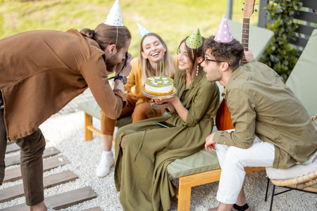 Friends having fun celebrating birthday party with a cake outdoors on nature. Man photographing with instant printing cameraの写真素材