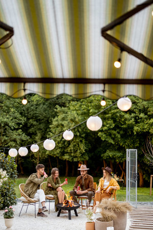 Friends having sitting by a fireplace, gathering together at backyard of the house in nature. View through the window from the insideの写真素材