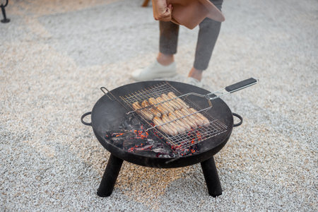 Man grilling sausages on a bbq bowl outdoors, close-up