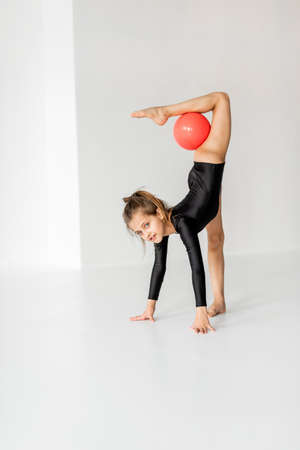 Little girl practising rhythmic gymnastic with a ball at white room. Childrens gymnastics and training from an early ageの写真素材