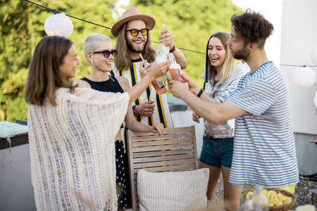 Young group of stylish people having a festive dinner on the roof terrace. Friends drinking beer and hanging out at picnicの写真素材
