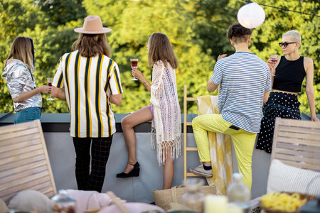 Young stylish people enjoy view on nature from the rooftop terrace, hanging out at party outdoors....