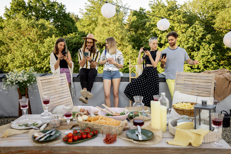 Young happy friends sitting in smartphones, spending time together on a rooftop terrace. Dependence...