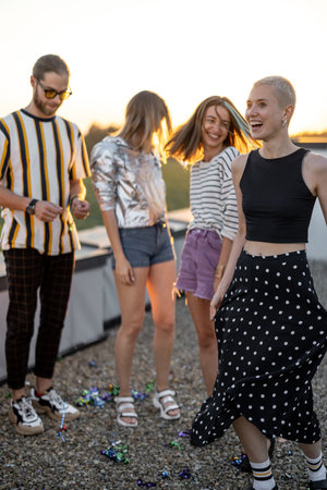 Young stylish friends dancing outdoors, having party at rooftop terrace on sunsetの写真素材