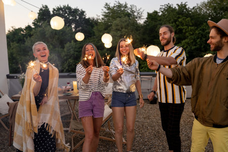 Young stylish people having fun, lighting sparklers during some celebration on a rooftop terrace at...
