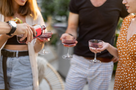 Young friends hanging out together with alcohol drinks at picnic outdoors. Close-up on glasses in...