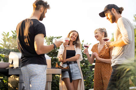 Young friends having fun at picnic outdoors, talk and drink wine at the backyard on a sunset. Spending summer time in a small group on the open airの写真素材