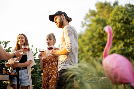 Young friends having fun at picnic outdoors, talk and drink wine at the backyard on a sunset....