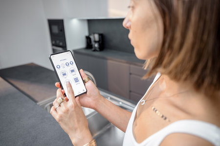 Female controlling smart kitchen devices with phone at home. Phone with running mobile application. Smart home conceptの写真素材