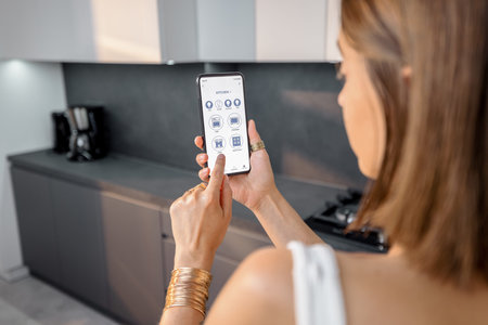 Female controlling smart kitchen devices with phone at home. Phone with running mobile application....