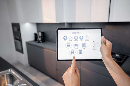 Digital tablet with running mobile application to control smart devices in the kitchen. Female controlling smart devices remotely at home. Smart home conceptの写真素材