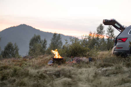 Beautiful picnic place near the car trunk with a campfire in the mountains on the eveningの写真素材