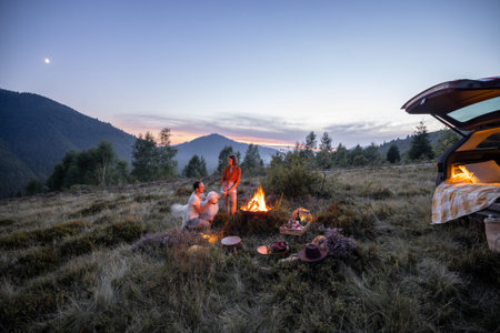 Couple sitting together with a dog by the fire, having romantic picnic, enjoying mountain landscapes...