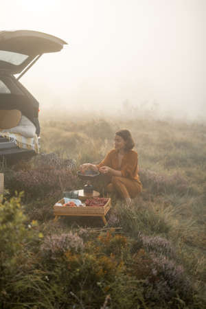 Woman traveler prepares breakfast, frying eggs on a burner while traveling in mountains on foggy weatherの写真素材