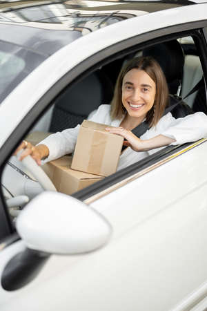 Young business woman drives a car with parcels in her hands. Concept of shopping online and picking up orders from the delivery office by carの写真素材
