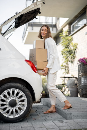 Young business woman picking up parcels from a car trunk, coming home by car. Concept of buying...
